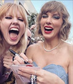 two women laugh as they take pictures with their cell phones and pen in front of them