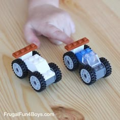 two lego cars sitting on top of a wooden table next to a hand reaching for one