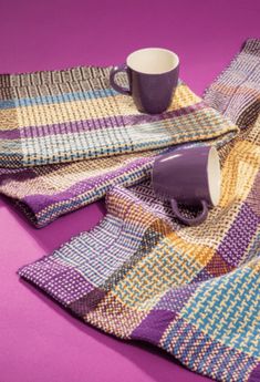 two mugs and a blanket on a purple surface