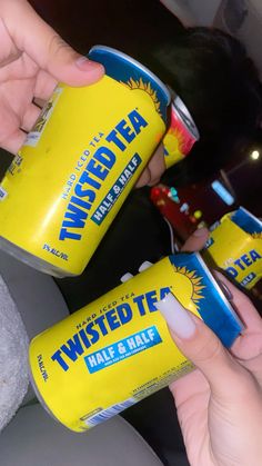 two cans of twisted tea are being held by someone's hand while sitting in a car