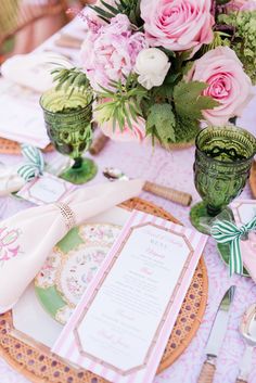 the table is set with pink roses and green vases, plates and napkins