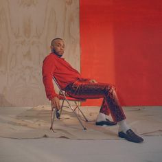 a man sitting on a chair in front of a red and white wall with his legs crossed