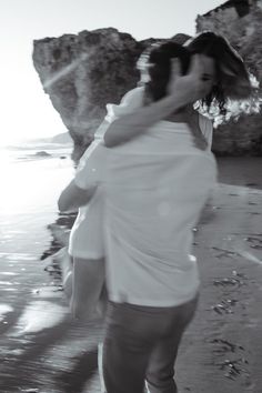 black and white photograph of two people hugging on the beach with rocks in the background