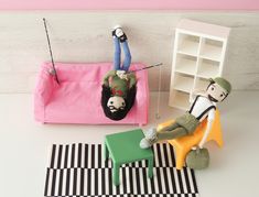 two dolls are sitting on the floor next to a pink chair and black and white checkered rug