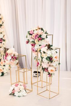 two gold stands with pink and white flowers on them, along with other floral arrangements