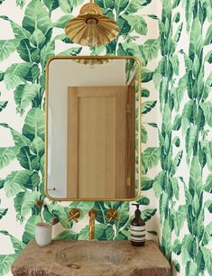 a bathroom sink under a mirror next to a wallpapered wall with green leaves