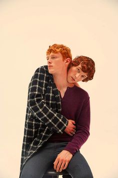 a man and woman sitting on top of a stool with their arms around each other