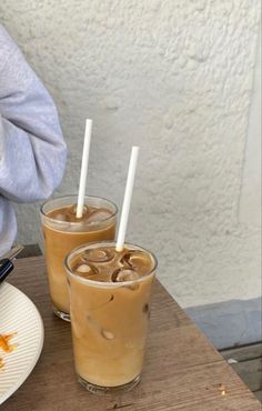 two beverages sitting on top of a wooden table next to a plate filled with food