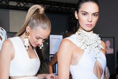 two women in white dresses standing next to each other at a fashion show with people looking on