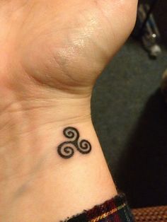 a small tattoo on the wrist of a woman's left hand, with an ornamental design