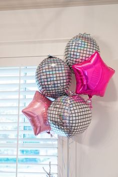 some pink and silver balloons are hanging on the wall in front of a window with shutters