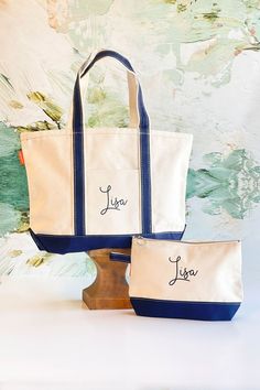 two personalized tote bags sitting next to each other on a wooden stand in front of a wall