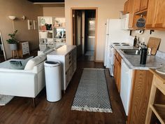 a living room and kitchen area with wood flooring, white couches and wooden cabinets