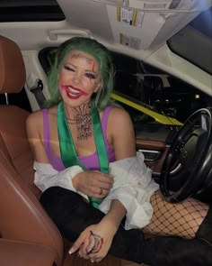 a woman with green hair and clown makeup sitting in the driver's seat of a car