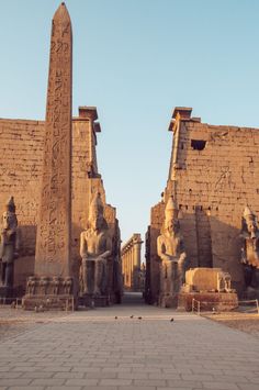 the entrance to an ancient egyptian temple with statues and obelisk on either side