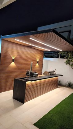 an outdoor kitchen with lights on the outside wall and grass in the front yard area