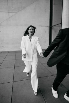 a man and woman holding hands walking down the street