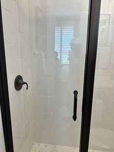 the shower door is open to reveal a white tiled bathroom with black handles and knobs