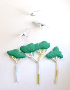 three green trees and two white birds flying in the air above them on a white wall