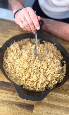 a person is stirring rice in a skillet with a spoon on a wooden table