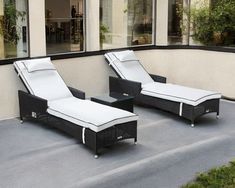 two black wicker lounge chairs with white cushions on a patio next to a building