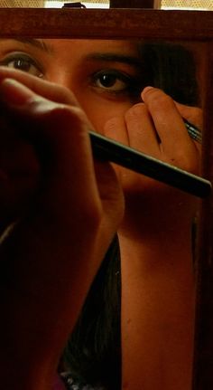 a woman holding a pen in front of her face and looking into the mirror with both hands