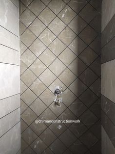 a tiled shower stall in a bathroom with grey and white tiles on the walls, along with a chrome faucet