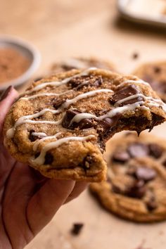 a hand holding a chocolate chip cookie with white icing