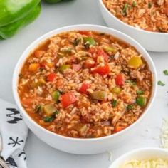 two white bowls filled with chili and rice next to green bell peppers on a table