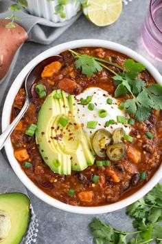 a white bowl filled with chili, avocado and sour cream on the side