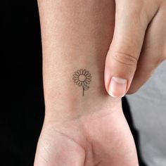 a woman's wrist with a small flower tattoo on the left side of her arm