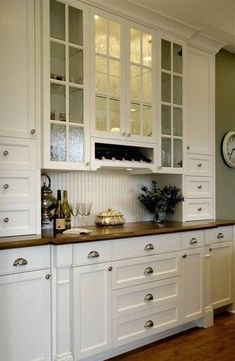 a kitchen with white cabinets and wood counter tops in front of a clock on the wall