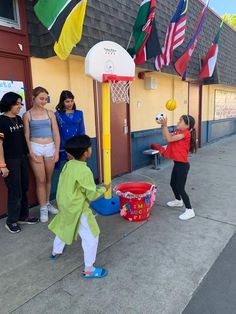 a group of young people standing around a basket ball game on a sidewalk next to a building