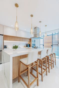 a kitchen with white counter tops and wooden stools next to an island in the middle