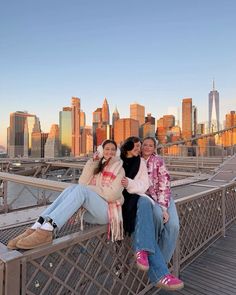 three women sitting on the edge of a bridge in front of a cityscape