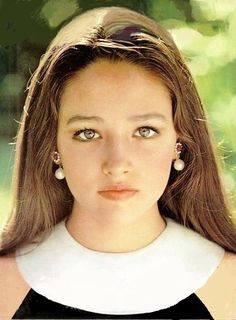 a close up of a person with long hair and wearing earring's in front of trees