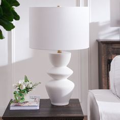 a white lamp sitting on top of a wooden table next to a white chair and potted plant