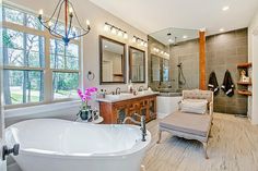 a large white bath tub sitting next to a sink in a bathroom under two windows