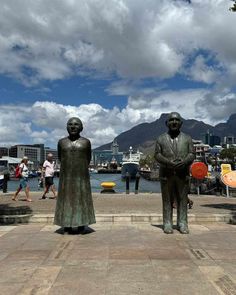 two statues of people standing next to each other in front of a body of water