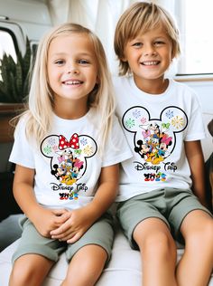 two young children sitting next to each other wearing mickey mouse tshirts and shorts