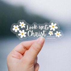 someone holding up a sticker with the words look into christ written in white and daisies