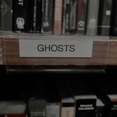 there is a sign that says ghosts on the shelf in front of bookshelves