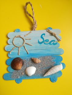 a wooden sign that says sea with shells on the sand and rope hanging from it