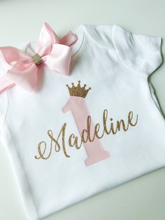 "1st birthday shirt includes a personalized baby bodysuit including the child's name and age as shown.  This does not include a tutu.  We offer white glove service with so many options to customize your order to meet your needs, creating the best memories of your baby girl's most precious milestones.  Read on for more details below. 💜 WHAT'S INCLUDED? 1) Personalized white bodysuit (*See note below regarding character limit)  2) Optional add-ons  - Satin hair bow on an elastic headband (Bow app Personalised 1st Birthday Gifts, Personalized Pink Tops For First Birthday, Personalized Pink Top For First Birthday, Custom Pink Tops For First Birthday, Mini Crown, 1st Birthday Shirts, First Birthday Shirts, Baby Girl First Birthday, 1st Birthday Gifts