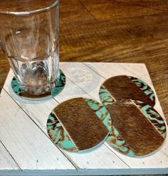 three coasters on top of a wooden table with a glass in the middle and another coaster behind them