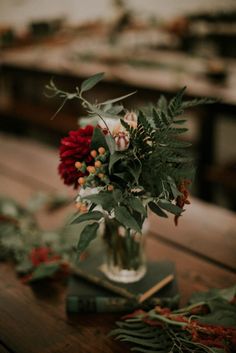 a vase filled with flowers sitting on top of a wooden table covered in leaves and berries