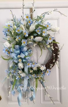 a wreath with blue and white flowers hanging on the front door, next to an open door