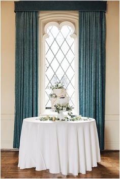 a wedding cake sitting on top of a white table in front of a large window