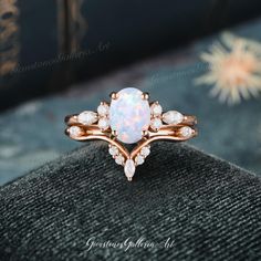 a white opal and diamond ring sitting on top of a black velvet cushion with flowers in the background