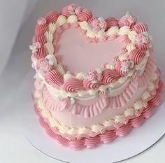 a heart shaped cake with pink frosting and white icing on a platter